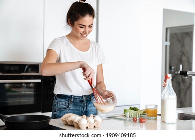 Happy brunette nice girl smiling while making scrambled egg at home kitchen - Powered by Shutterstock