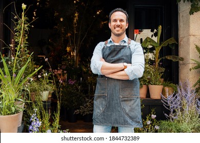 Happy Brunette Spanish shopkeeper is smiling while holding a beautiful plant pot at the storefront of his florist