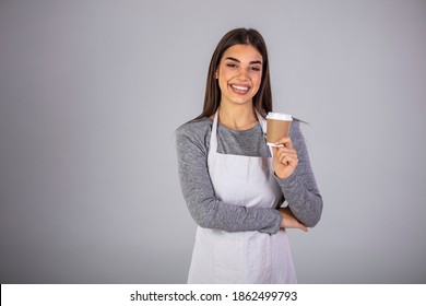 Happy brunette waitress in apron offering you glass with hot coffee while standing in front of camera in isolation. A waitress holding and serving a paper cup of hot coffee