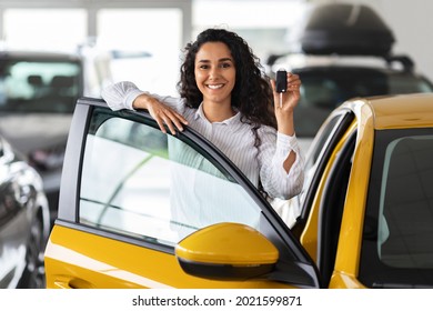 Happy brunette woman buying new cute car, raising hand up with automatic key and smiling, showroom interior, copy space. Pretty curly lady customer purchasing yellow female auto, getting in - Shutterstock ID 2021599871