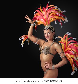 Happy Brunette Woman In Carnival Suit With Rhinestones And Feathers. Beautiful Showgirl With Professional Make-up On A Black Background. Copy Space.