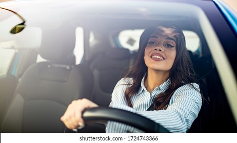 Happy brunette woman driving a car. Portrait of beautiful caucasian woman with toothy smile and brown hair driving car. Hand on steering wheel. Young woman driving a car in the city 