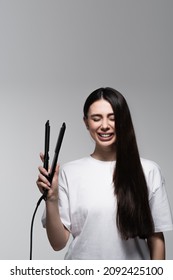 Happy Brunette Woman Holding Hair Straightener Isolated On Grey