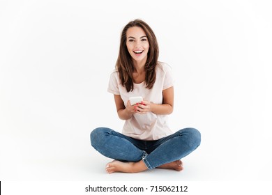 Happy brunette woman holding smartphone in hands and looking at the camera over white background