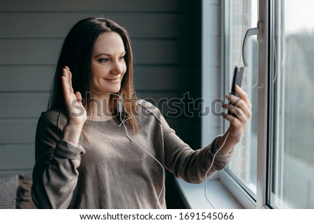 Happy brunette woman at home making facetime video calling with smartphone at home, using zoom meeting online app, social distancing, work from home, work remotely concept
