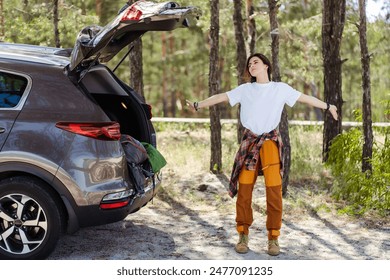 Happy brunette woman stretching hands near car in forest during vacation. Traveling by car, active lifestyle concept - Powered by Shutterstock