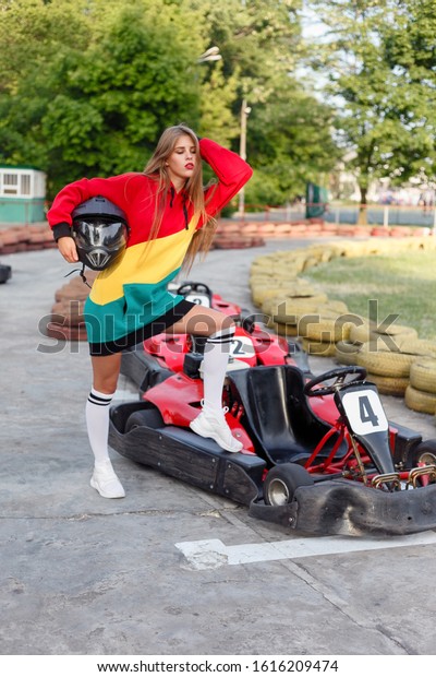 happy\
brunette women wining the karting race. oung blonde girl in red\
sports suit posing in summer on a kart\
track