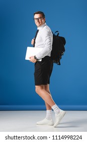 Happy Buisnessman In Eyeglasses And Shorts Holding Laptop And Smiling At Camera On Blue