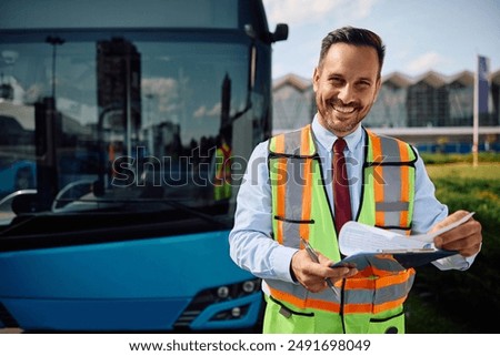 Happy bus driver going through driving schedule at the station and looking at camera.