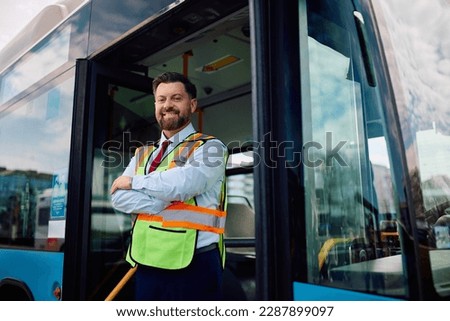 Happy bus driver standing at the entrance of a vehicle with his arms crossed and looking at the camera. Copy space.