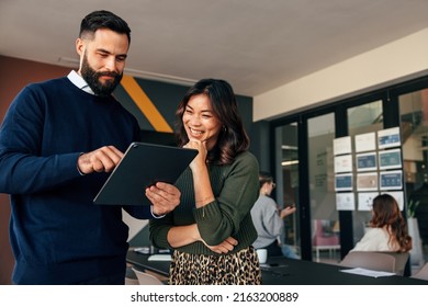 Happy business colleagues using a digital tablet in a boardroom. Two young businesspeople having a discussion during a meeting. Diverse entrepreneurs working together as a team. - Shutterstock ID 2163200889