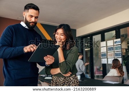 Happy business colleagues using a digital tablet in a boardroom. Two young businesspeople having a discussion during a meeting. Diverse entrepreneurs working together as a team.