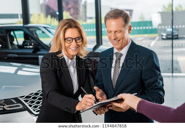 happy business couple signing papers for buying\
new car in showroom