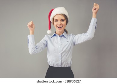 Happy business lady in Santa hat is looking at camera and smiling while celebrating New Year, on gray background - Powered by Shutterstock