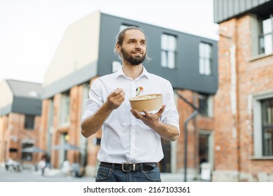 Happy Business Man Eating Healthy Salad On A Break Standing Over City Street Background. Male Dieting Nutrition Concept. Attractive Smiling Guy Enjoying Veggie Meal.