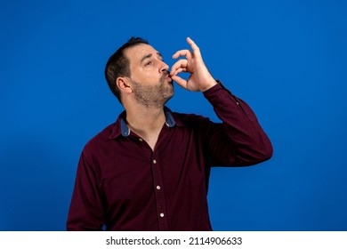 Happy Business Man Licking Fingers Isolated On Blue Studio Background. Beautiful Male Half-length Portrait. Young Satisfy Man. Human Emotions, Facial Expression Concept. Front View