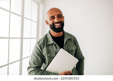 Happy business man standing in an office holding a laptop. Professional man smiling and enjoying being at work.