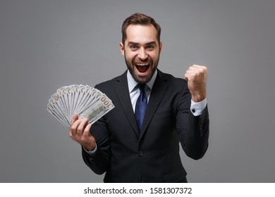 Happy Business man in suit shirt tie posing isolated on grey background. Achievement career wealth business concept. Mock up copy space. Hold fan of cash money in dollar banknote doing winner gesture