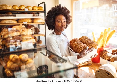 Happy business owner at a bakery shop. Young bakery owner holding a tray with bread in her shop. Beautiful baker. Happy woman working at the bakery and looking at the camera smiling - small business - Shutterstock ID 1804432549