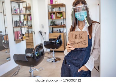 Happy business owner at a hairdressing studio hanging an OPEN sign during COVID-19. Local business in Europe reopening post pandemic. Portrait shot of a local business owner hanging an OPEN sign 