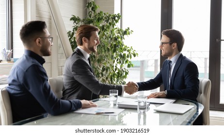 Happy business partners shaking hands, greeting or making successful great commercial deal after successful negotiations, smiling diverse employees sitting at table in modern boardroom, acquaintance