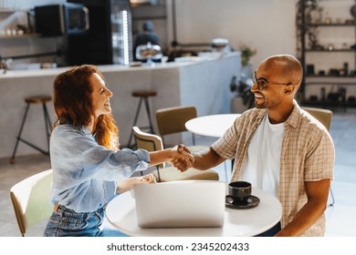 Happy business partners shaking hands during a lunch meeting in a coffee shop. Two successful business people, a woman and her client, come to an agreement and close a business deal. - Powered by Shutterstock