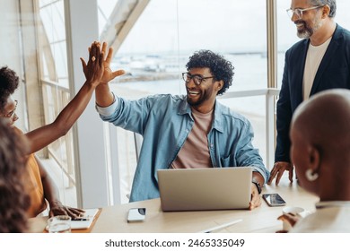 Happy business people celebrating teamwork in a boardroom. Business people high-fiving, showcasing success. Utilizing technology, working on a successful project in a modern office setting. - Powered by Shutterstock