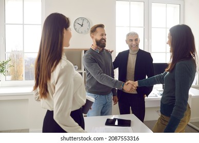 Happy business people meeting in a modern office. Two colleagues making an acquaintance and greeting each other. Friendly man and woman shaking hands after their coworkers have introduced them - Shutterstock ID 2087553316