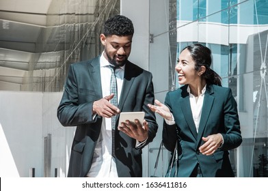 Happy Business People Talking And Walking Along Street. Business Man And Woman Wearing Formal Clothes And Using Tablet Computer With Building In Background. Business People Concept. Front View.