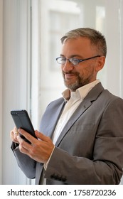 Happy Business Person Touching Screen Of His Smart Phone. Handsome Mature Businessman Using Mobile Phone.  Portrait Of Smiling Middle Aged Businessman With Cell Phone.