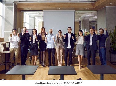 Happy Business Team Celebrating Great Achievements And Teamwork. Multriacial Group Of Cheerful Colleagues Standing By Office Projection Screen Cheering After Successful Presentation At Work Meeting