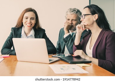 Happy business team watching project presentation on laptop, sitting at meeting table with paper reports and diagrams. Medium shot. Marketing and teamwork concept - Shutterstock ID 1914778942