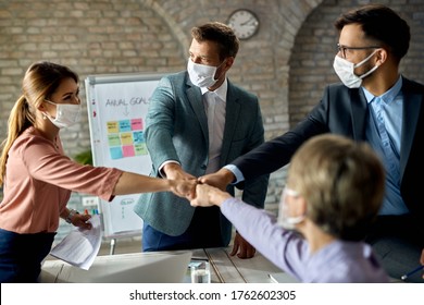 Happy business team wearing protective face masks while colliding their fists on a meeting in the office.  - Powered by Shutterstock