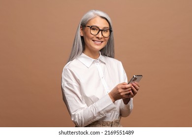 Happy business woman in formal shirt touching to the smartphone screen while feeling great with new phone features. Indoor studio shot isolated on beige background