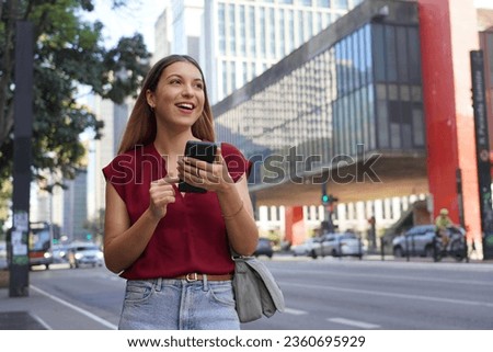 Happy business woman looking away with her smartphone walking on Paulista Avenue, Sao Paulo, Brazil