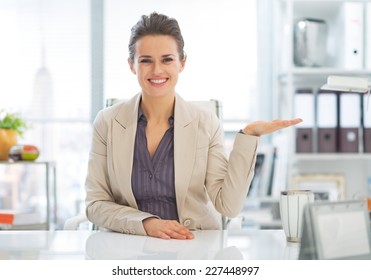 Happy Business Woman Presenting Something On Empty Palm In Office