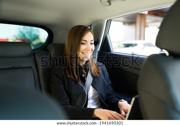 Happy business woman\
smiling while working on her laptop during a ride on a taxi cab of\
a ride-share app. Busy businesswoman typing on the computer in the\
back of a car