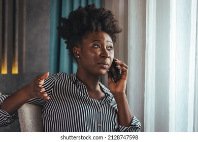 A Happy Business Woman Is Talking On A Mobile Phone While Sitting At The Table Of A Hotel Room With A Laptop. A Female CEO On A Business Trip Works From A Hotel Room.