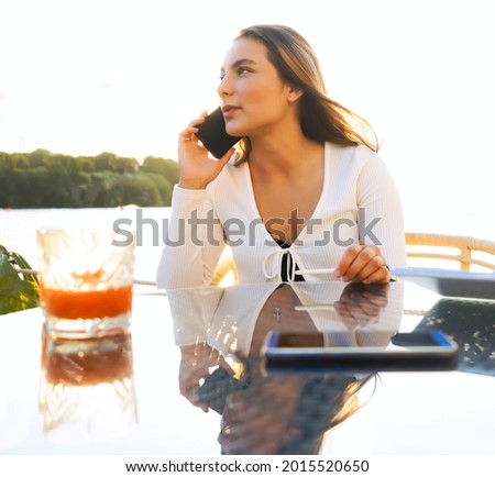 Happy business woman talking the phone sitting in outdoors cafe in european city. Sunny summer day
