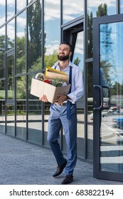 happy businessman with cardboard box walking out office building, quitting job concept