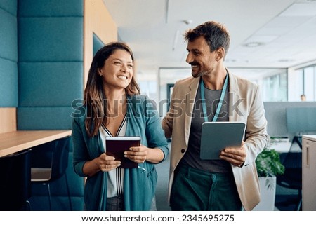Happy businessman communicating with female colleague while walking through the office.