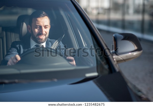 Happy businessman driving a luxury car, view\
from the outside through the\
windshield
