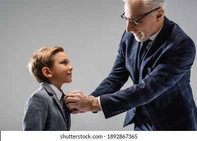 happy businessman in eyeglasses buttoning blazer of smiling grandson isolated on grey - Shutterstock ID 1892867365