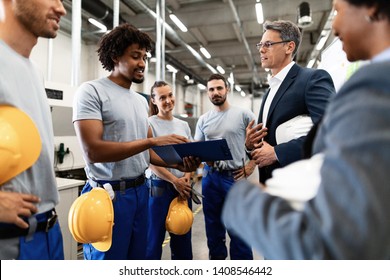 Happy businessman and factory workers communicating while going through reports in industrial building.  - Powered by Shutterstock