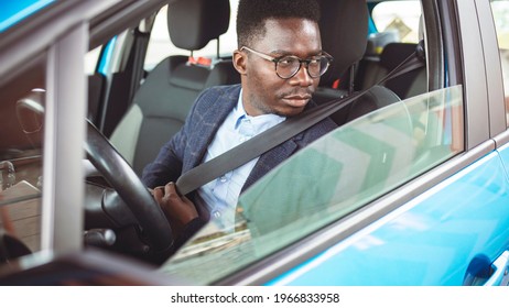 Happy Businessman Fastening Seatbelt Before His Trip By Car. Portrait Of Young African Man Sitting In Driving Seat Of Car, Fastening Safety Belt. Safety First. Man Buckling Her Seatbelt In Car