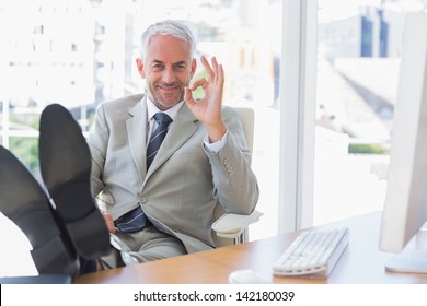 Happy Businessman Giving Ok Sign With Feet Up On His Desk