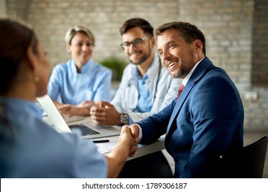 Happy businessman having a meeting with group of doctors and shaking hands with one of them in the office. 