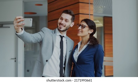 Happy businessman and his female colleague taking a selfie on smarphone camera for social media in modern office indoors