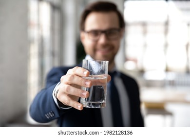 Happy businessman holding glass of fresh filtered cold water, toasting at camera. Male employee drinking still mineral water during break, keeping hydration aqua balance. Close up of hand - Powered by Shutterstock