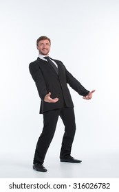 Happy Businessman Holding An Invisible Heavy Load On His Back Isolated On White. Smiling Man In Black Business Suit Wants To Succeed.